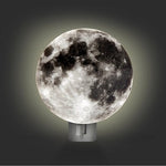 Load image into Gallery viewer, An image of the moon night light in a dark room. The night light is illuminated behind a circular cardboard image of the lunar surface to give the impression that the moon is glowing.
