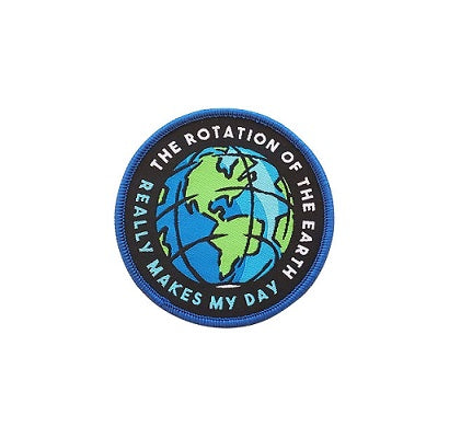 A circular iron on patch with a graphic of a spinning earth in the centre. Around the earth, there is blue and white text that reads "The rotation of the Earth really makes my day"
